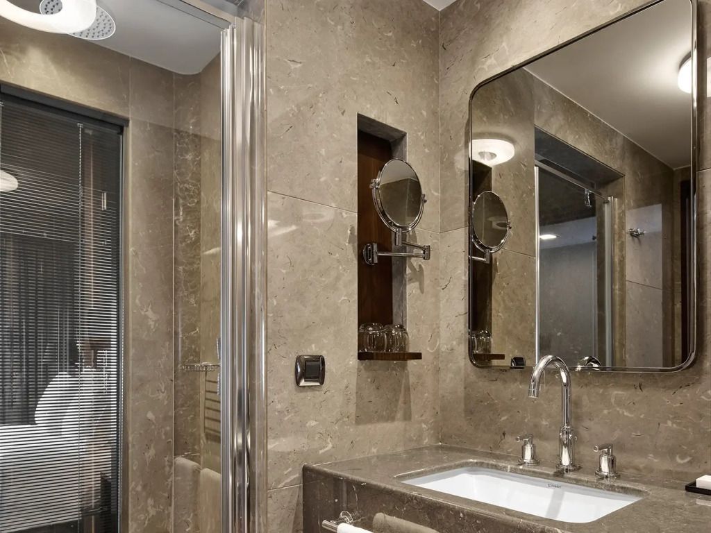 Modernes Badezimmer mit edler Marmorverkleidung und großzügigem Spiegel.