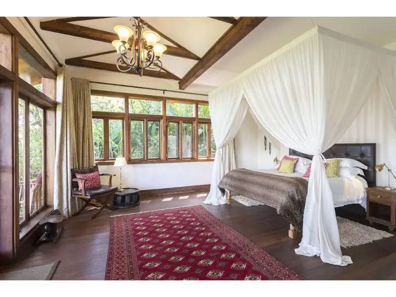 Geräumiges Schlafzimmer mit Himmelbett und großen Fenstern, die den Garten überblicken