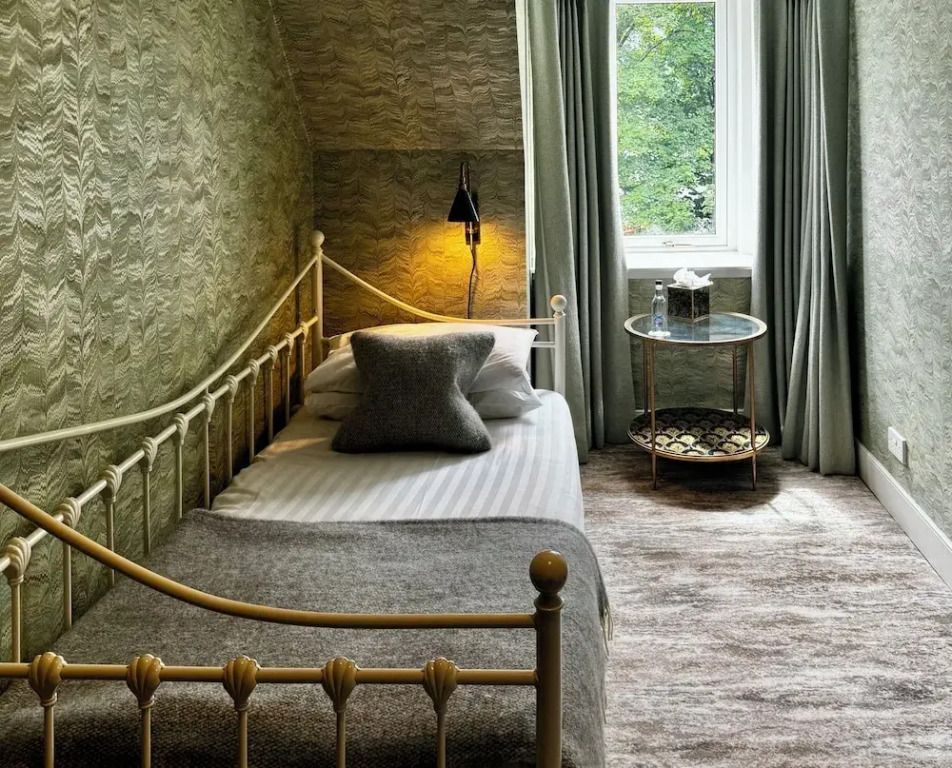 Einzelbett in einem gemütlichen Zimmer mit Tisch und Lampe am Fenster