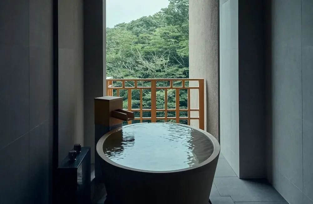 Runde Badewanne mit Wasser und Aussicht auf Wald durch offenes Fenster