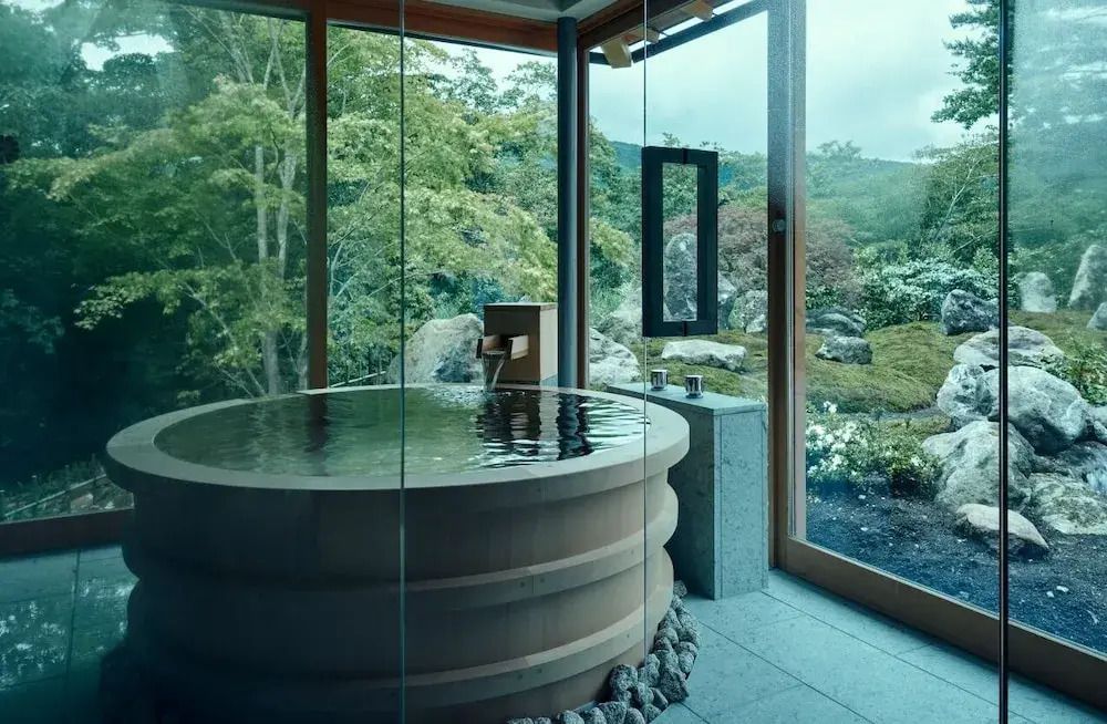 Privater Onsen mit Glaswänden und Blick auf einen üppigen Garten