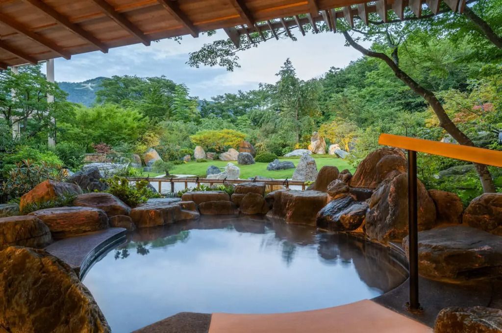 Onsen im Freien mit Blick auf gepflegten japanischen Garten und grüne Landschaft