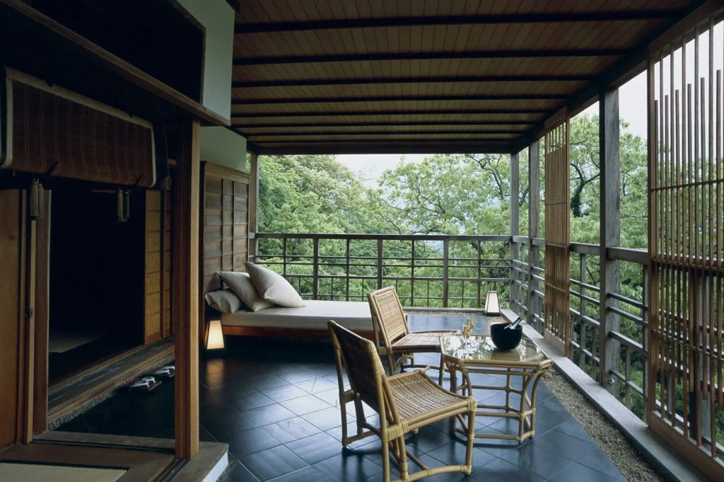 Balkon mit Holzverkleidung, Rattanmöbeln und subtilem Blick auf eine bewaldete Landschaft.