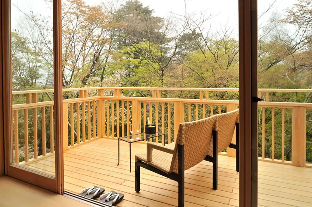 Holzbalkon mit zwei Stühlen und Blick auf umliegende Bäume.