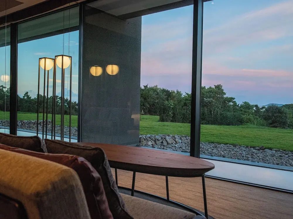 Sitzecke mit Blick auf einen grünen Garten durch große Fenster bei Sonnenuntergang