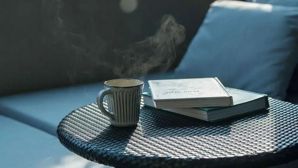 Dampftasse auf Tisch neben Büchern auf Balkon mit entspannter Atmosphäre