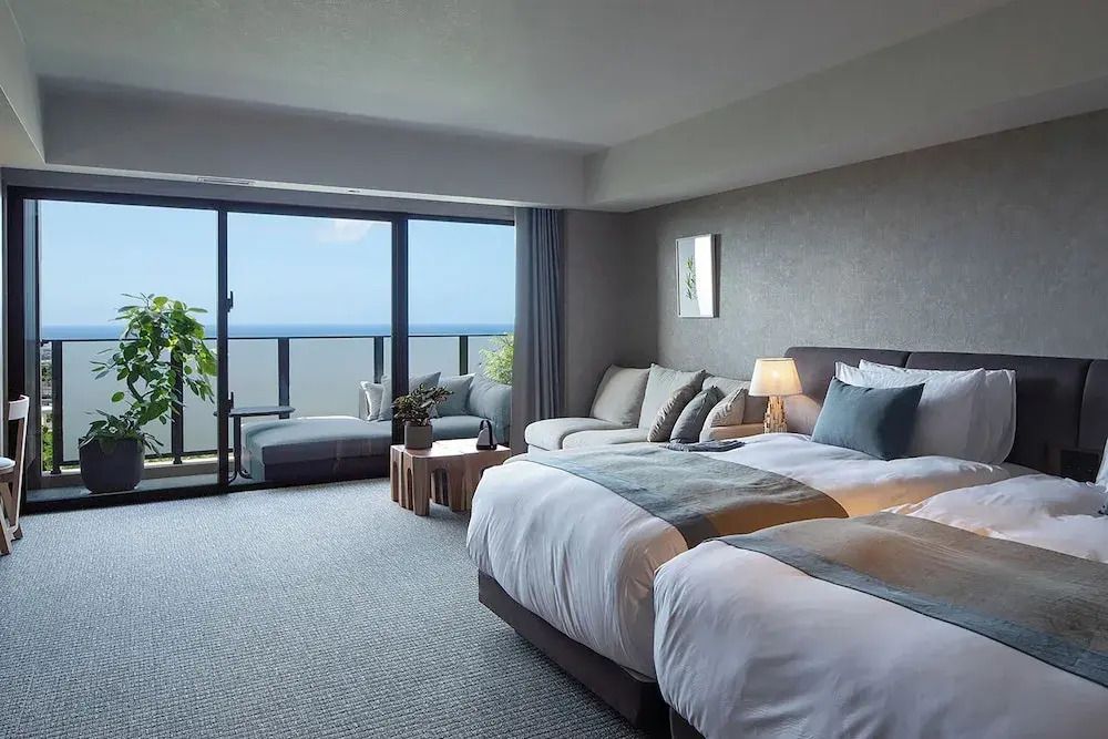 Elegantes Hotelzimmer mit Doppelbett, Sofa und Balkon mit Meerblick.