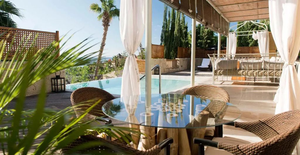 Terrasse mit Poolblick und stilvollen Sitzmöglichkeiten unter blauem Himmel.
