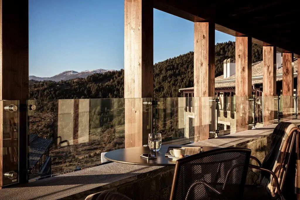 Balkon mit Glasgeländer, Blick auf Berge und Wälder, Tisch mit Kaffee