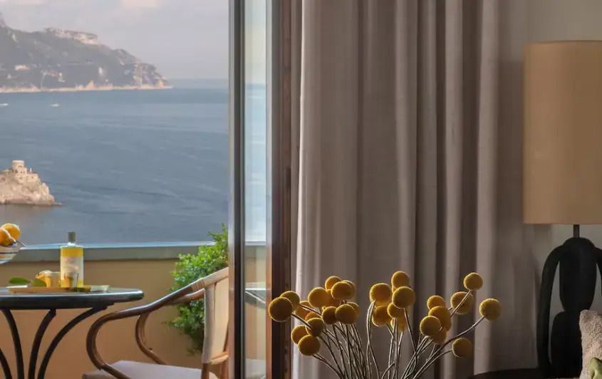 Blick durch ein Fenster mit Blick auf das Meer und gelbe Blumen im Vordergrund.