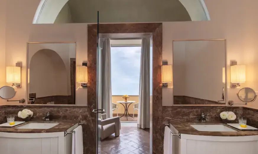 Badezimmer mit Marmorakzenten und einem Balkon mit Meerblick.