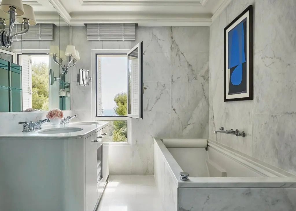 Helles Badezimmer aus Marmor mit Badewanne und offenem Fenster mit Aussicht.