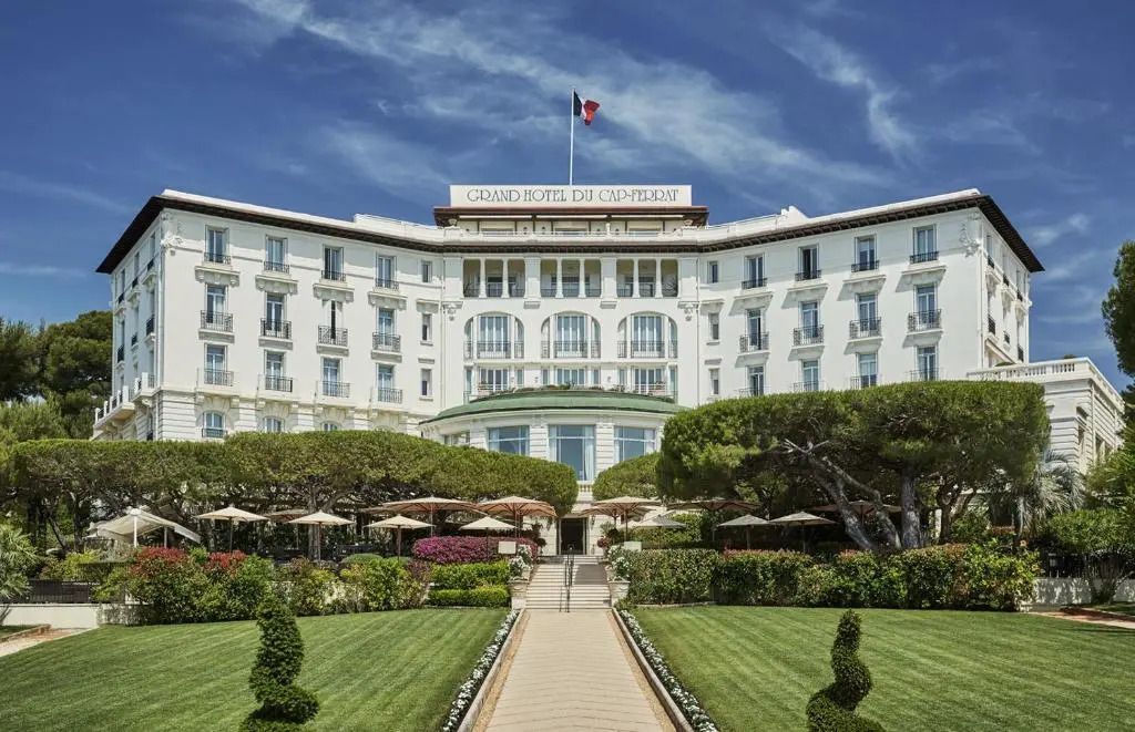 Prachtvolle Fassade des Grand-Hôtel du Cap-Ferrat mit gepflegtem Garten und französischer Flagge.