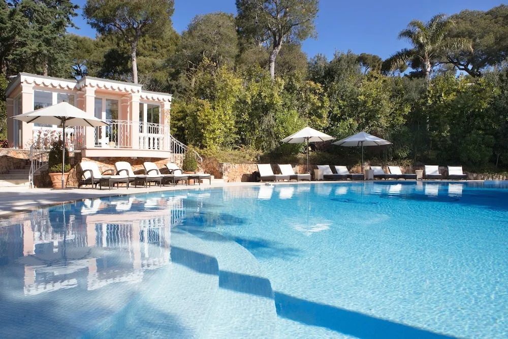 Blauer Pool mit Sonnenliegen und Gartenblick unter klarem Himmel.