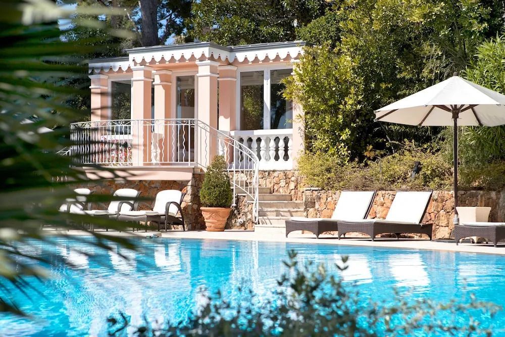 Poolbereich mit Liegestühlen und klassischer Villa im Hintergrund.