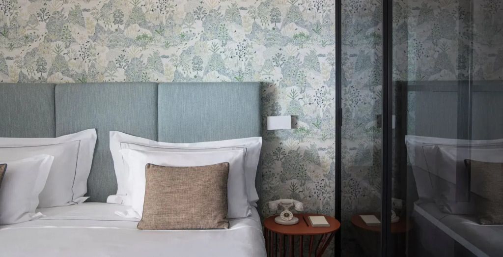 Komfortables Bett mit dekorativen Kissen und botanischer Tapete im Hotelzimmer