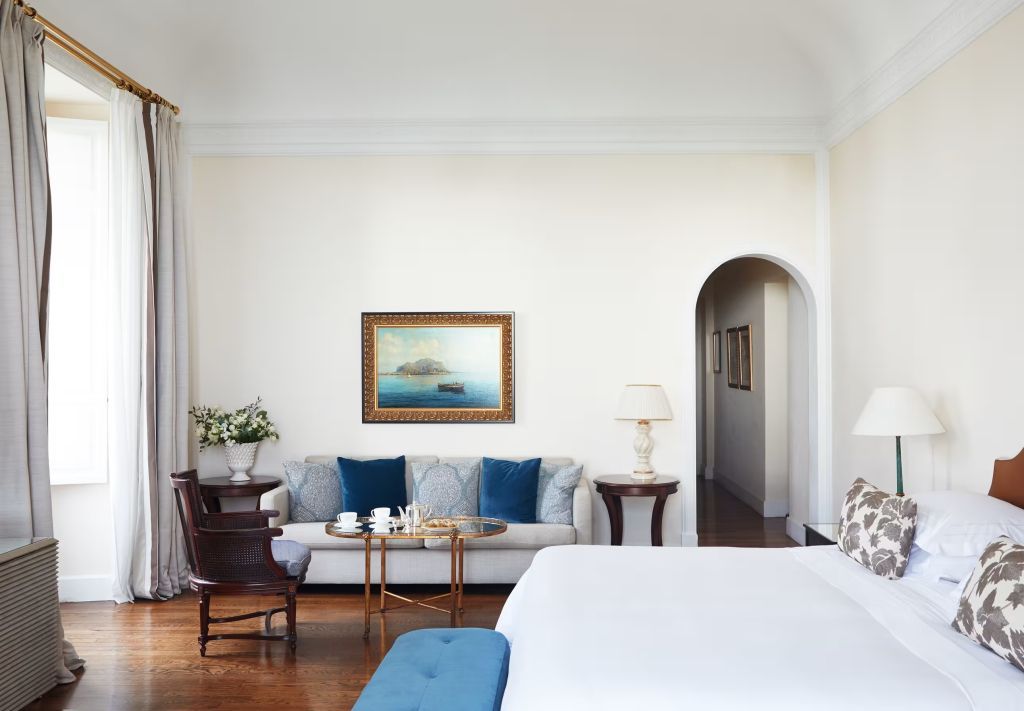 Weißes Bett in Deluxe Junior-Suite. Komfortabler Wohnbereich mit blauen Akzenten.