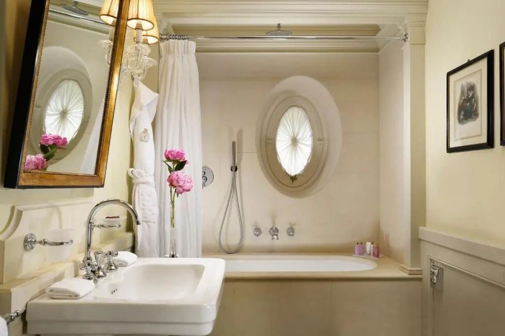 Helles Badezimmer mit stilvollem Waschbecken und ovalem Fenster in der Junior-Suite
