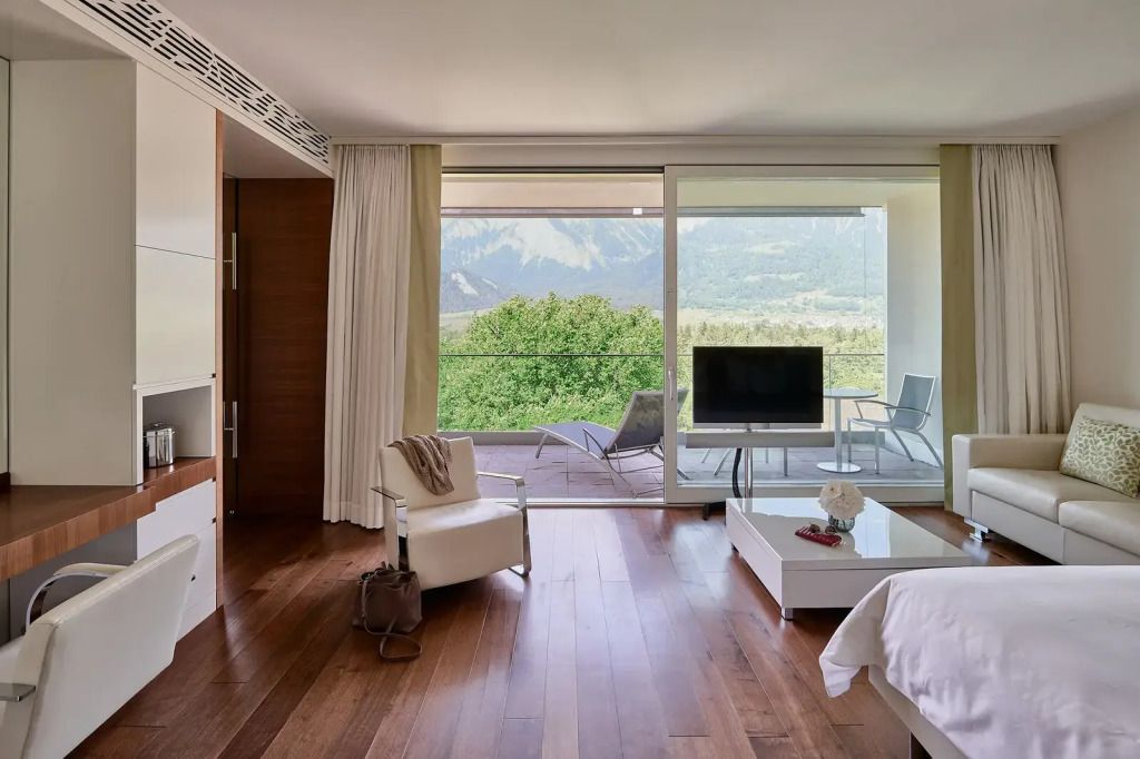 Zimmer mit Holzboden, Fernseher und Panoramafenster mit Blick auf die Berge