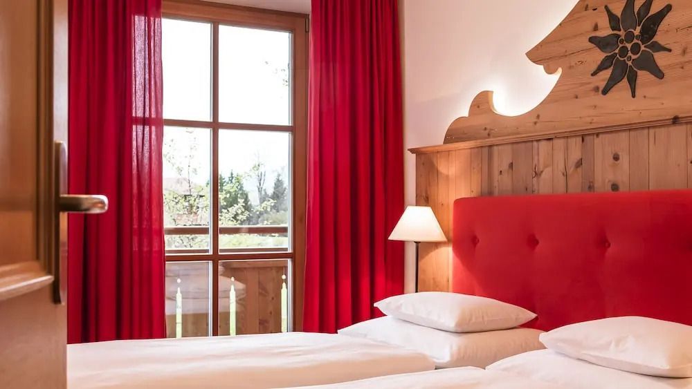 Helles Zimmer mit Blick auf den Balkon durch große Fenster und rote Vorhänge.
