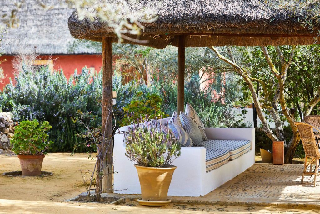 Schattige Gartenlounge mit Sitzbank unter einem Strohdach