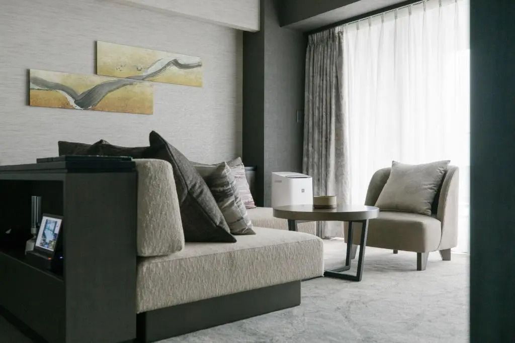 Sitzbereich mit Sofa und Sessel neben großen Fenstern mit Vorhängen