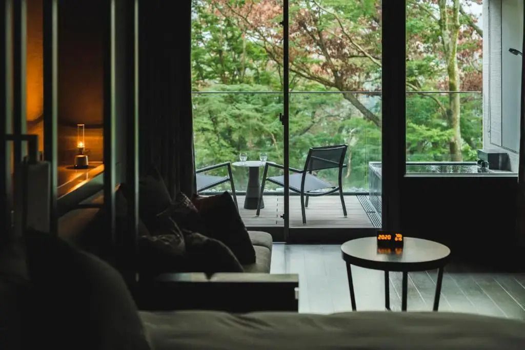 Sitzbereich mit Blick auf Balkon und grüne Bäume im Deluxe-Zimmer mit Offenbad