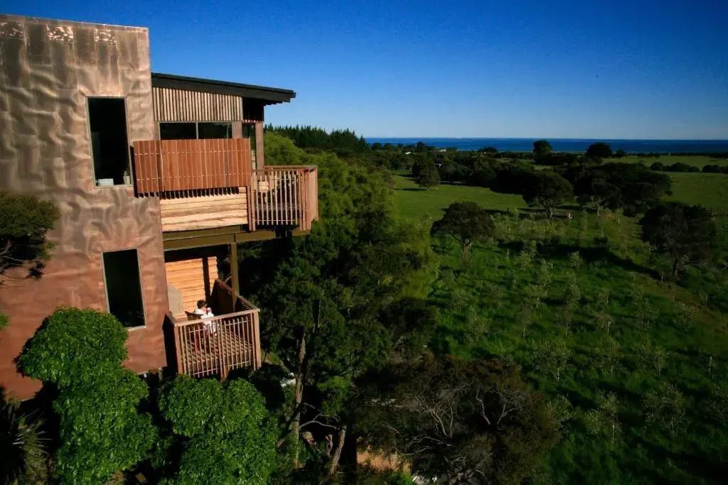 Blick auf die Baumhaus-Struktur mit Balkon und grüner Landschaft mit Meer im Hintergrund.