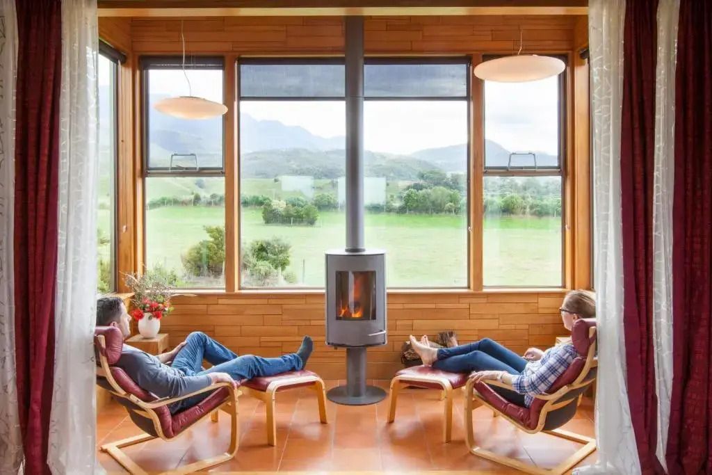 Paar entspannt auf Stühlen vor einem Kamin mit Panoramafenster.