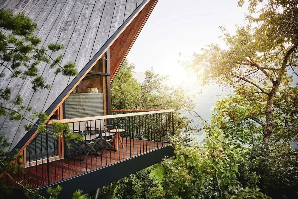 Balkon eines Chalets mit Blick auf grüne Landschaft und Bäume im Sonnenlicht.