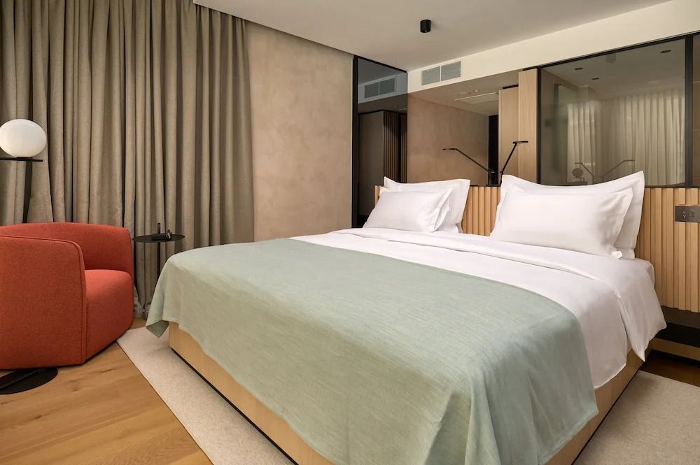 Elegantes Zimmer mit modernem Doppelbett, grüner Überdecke und gemütlichem Stuhl.