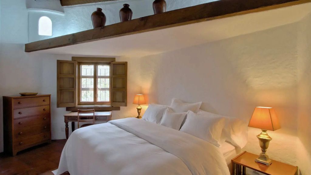 Elegantes Schlafzimmer mit großen Kissen und einem Fenster mit Blick ins Grüne.
