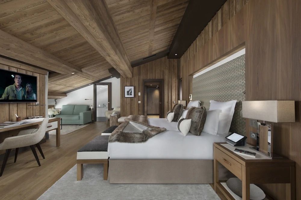 Elegantes Zimmer mit Doppelbett und Sesseln unter einer Holzdecke aus hellem Holz.