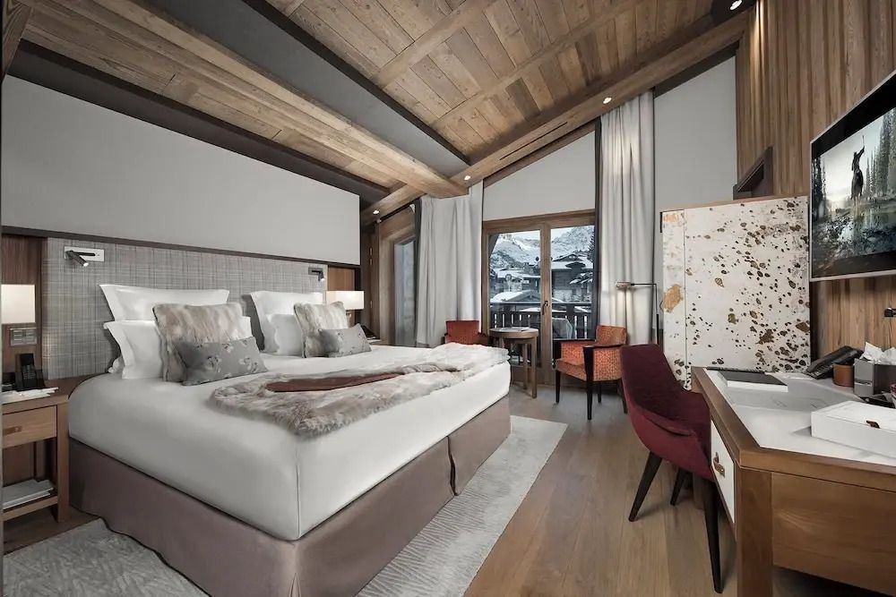 Modernes Zimmer mit großem Bett, Arbeitsbereich und Aussicht auf verschneite Berge.