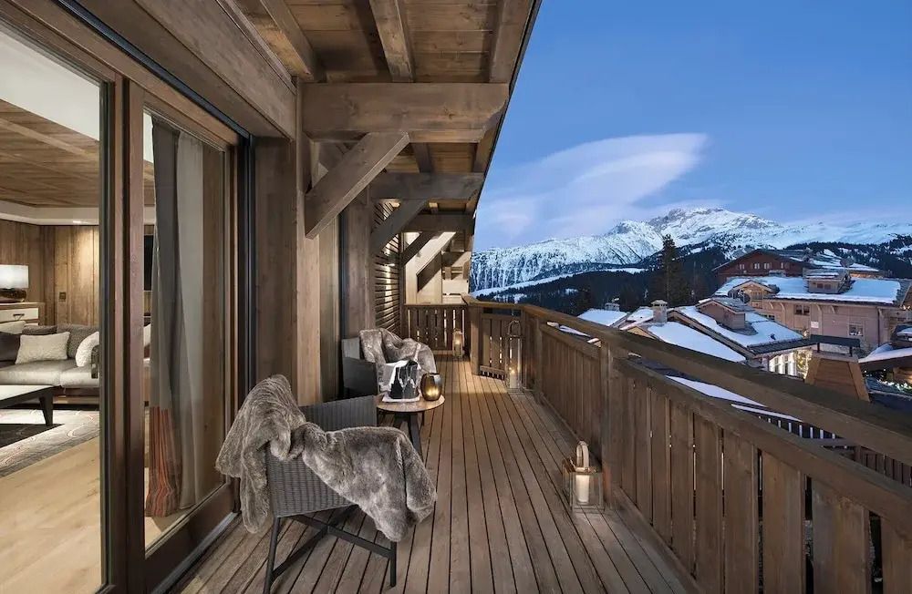 Holzbalkon mit bequemen Stühlen und Blick auf verschneite Berge.