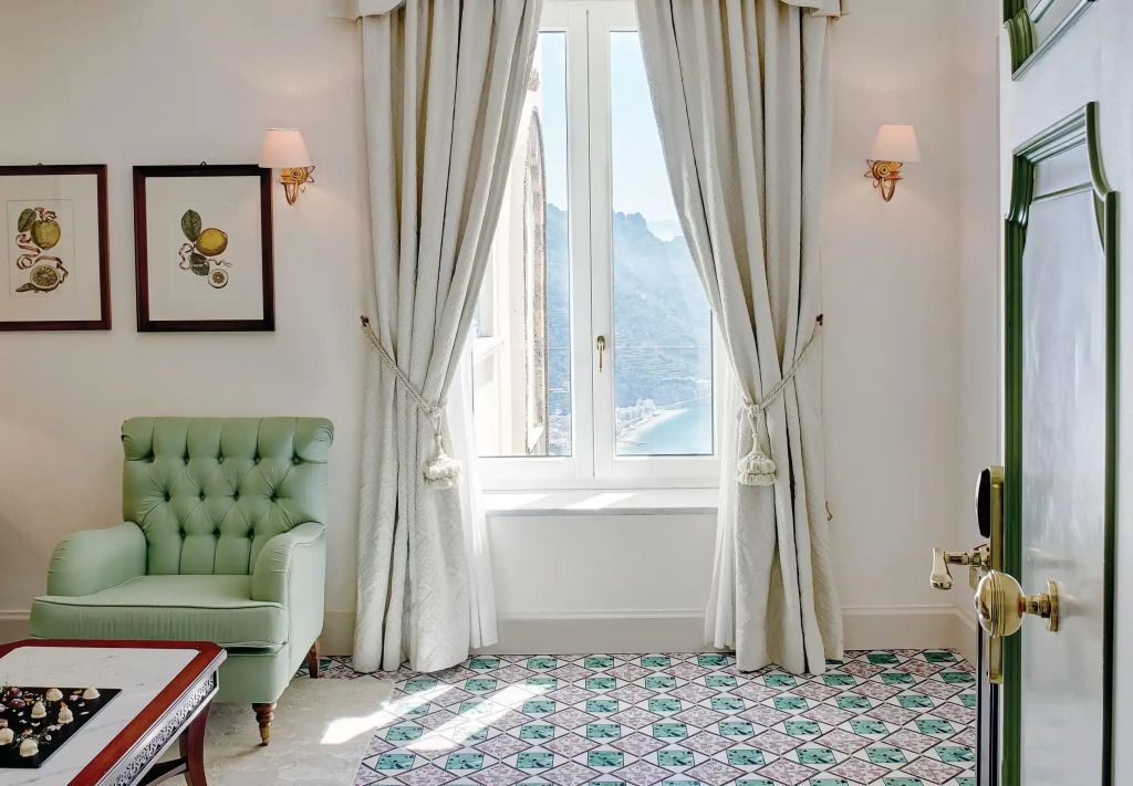 Heller Raum mit Ausblick auf die Küste durch ein Fenster mit Vorhängen im Caruso Hotel