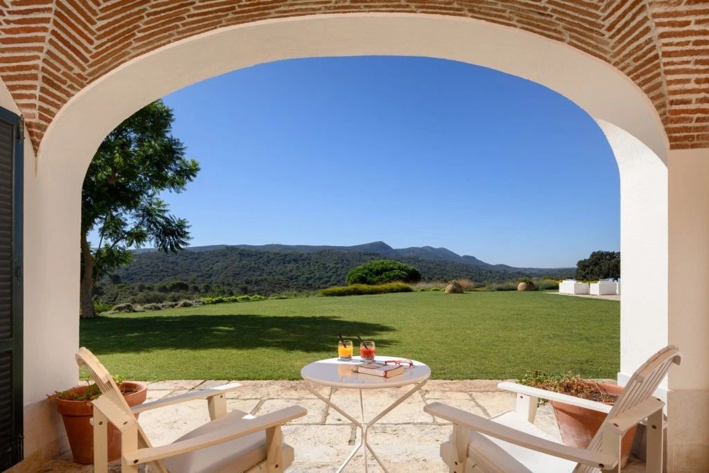 Sonnige Terrasse mit Sitzgelegenheiten und freiem Blick auf grüne Landschaft und blauen Himmel.