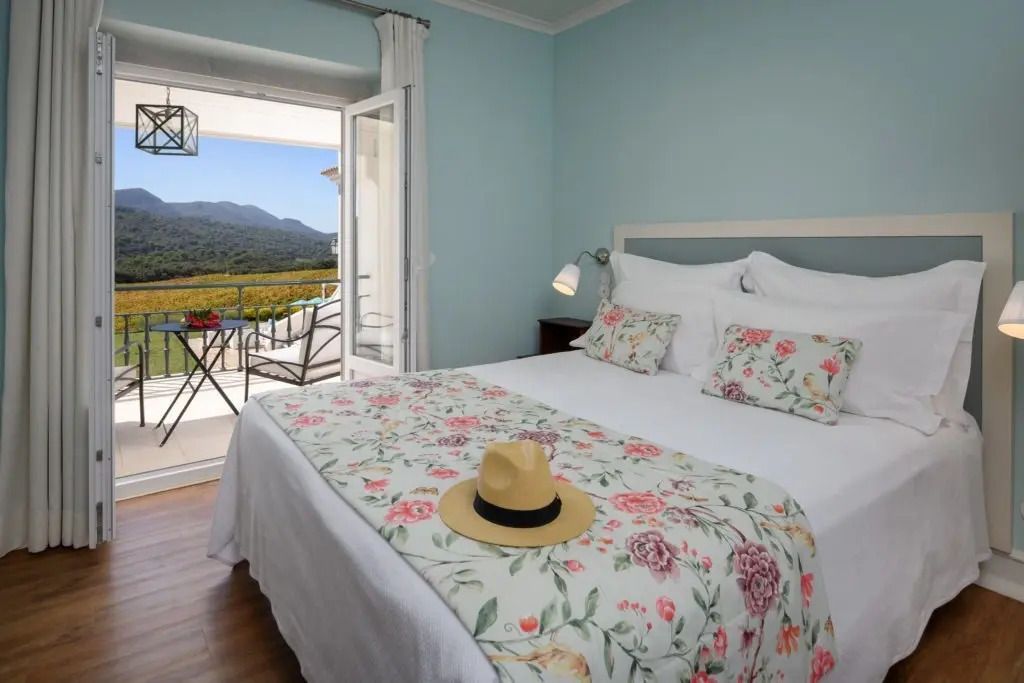 Premium-Zimmer mit floralem Bettbezug, Hut auf dem Bett und Balkon mit Aussicht.