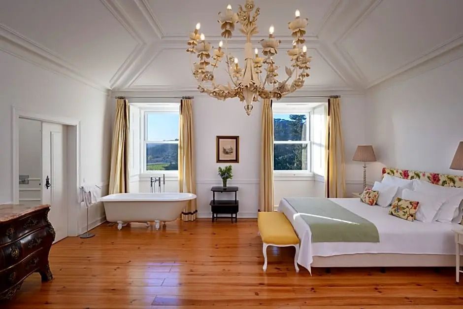 Helles Schlafzimmer mit Kronleuchter, Holzboden und freistehender Badewanne