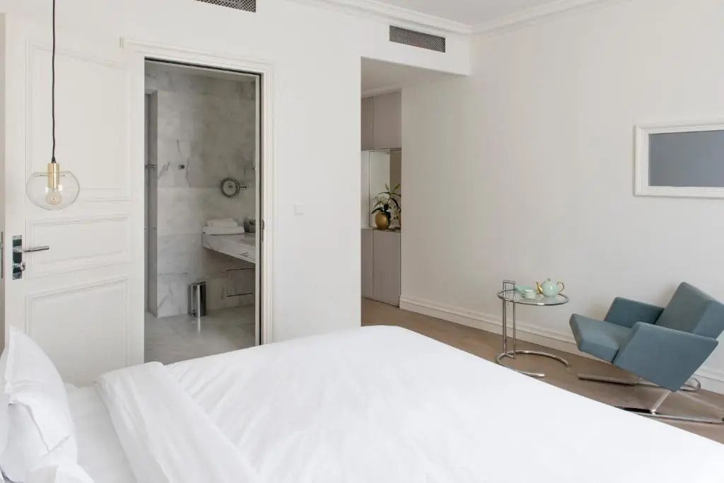 Blick vom Bett auf ein Badezimmer mit offener Tür und einem kleinen Tisch