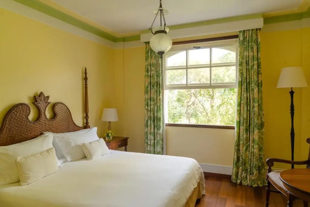 Schlafzimmer mit Doppelbett, eleganter Beleuchtung und großen Fenstern mit Blick ins Grüne