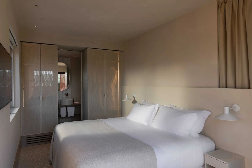 Modernes Schlafzimmer in neutralen Farben mit großem Doppelbett und Bad im Hintergrund.