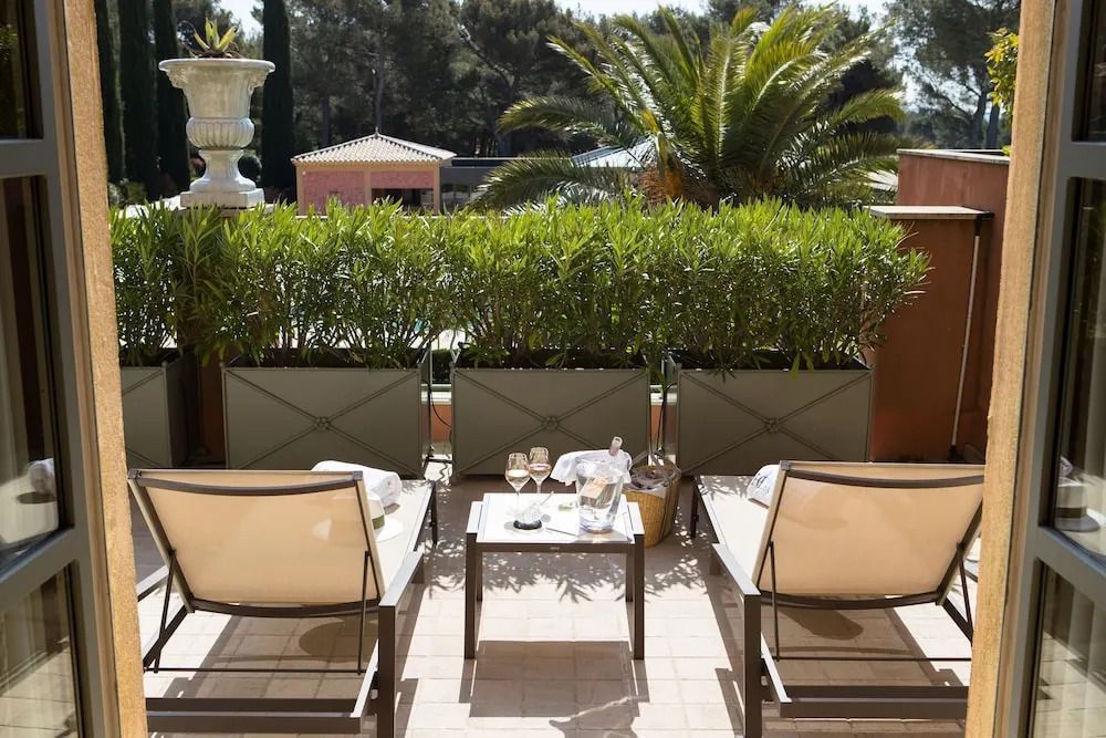 Sonniger Balkon mit Sitzgelegenheiten und Blick auf üppiges Grün und Palmen.