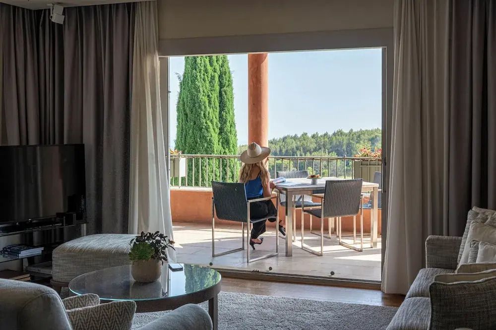Frau mit Hut sitzt auf Balkon mit Tisch und Blick auf Natur