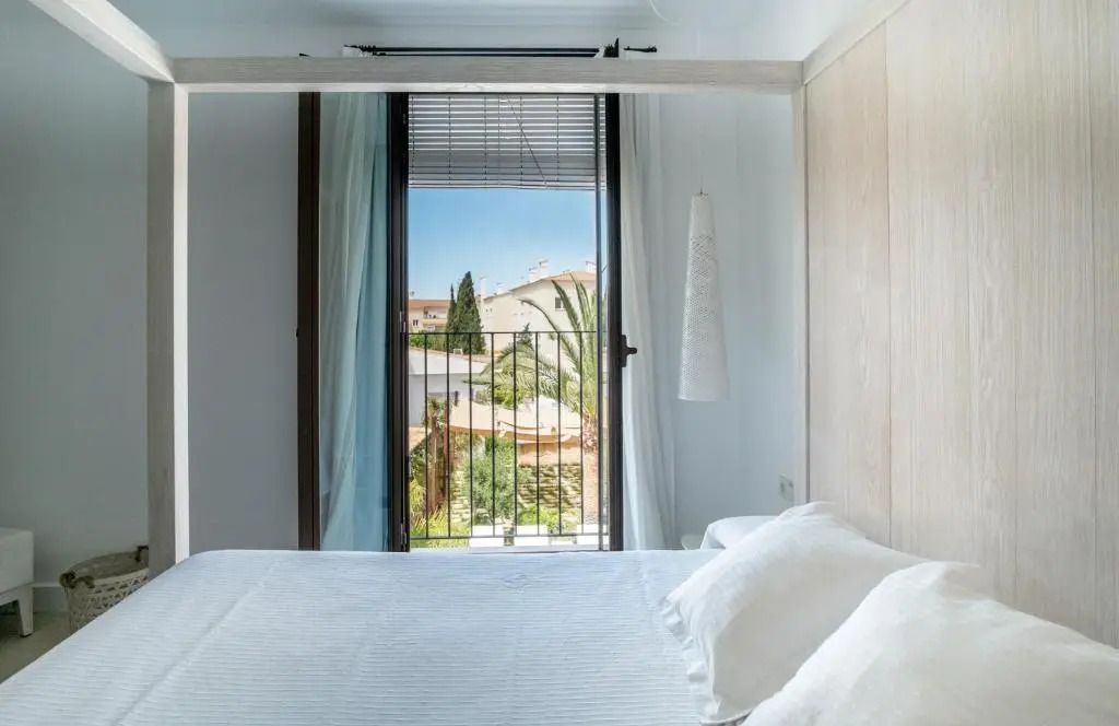 Modernes Hotelzimmer mit Doppelbett und Blick auf einen Balkon mit Palmen.