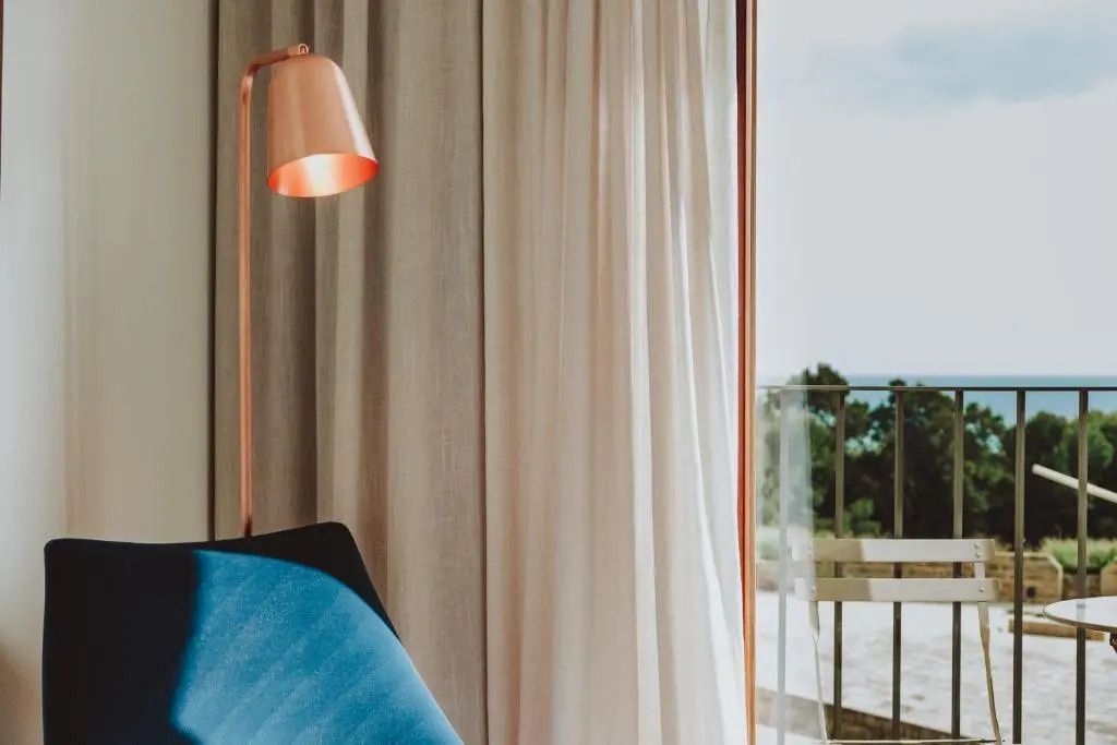 Elegante Stehleuchte und Vorhänge neben großem Fenster mit Naturblick.