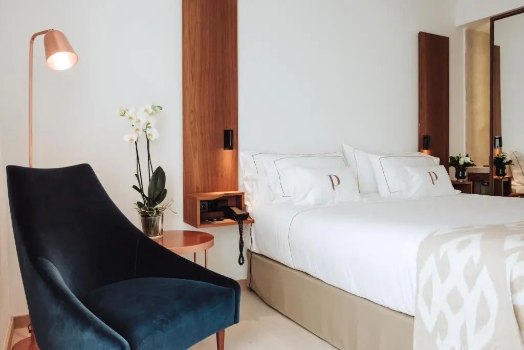 Moderne Einrichtung mit komfortablem Bett, Holzdetails und eleganter Sitzgelegenheit.