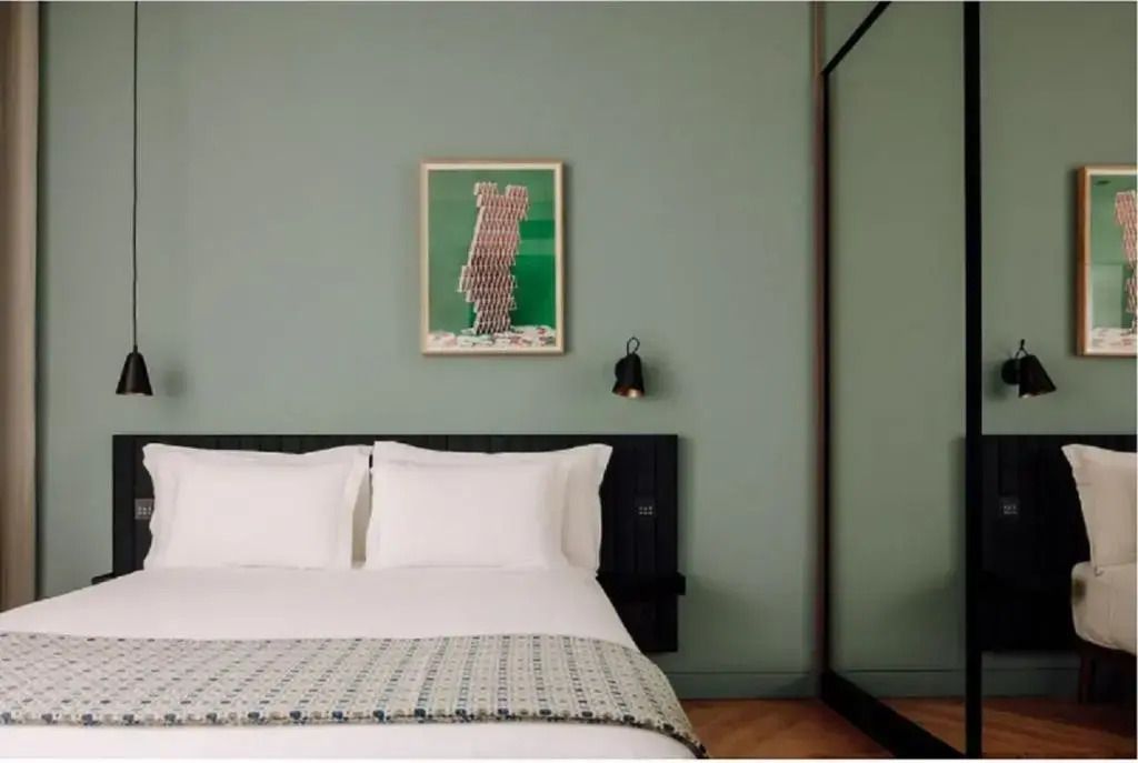 Doppelbett im modernen Zimmer mit grüner Wand und stilvoller Kunst.