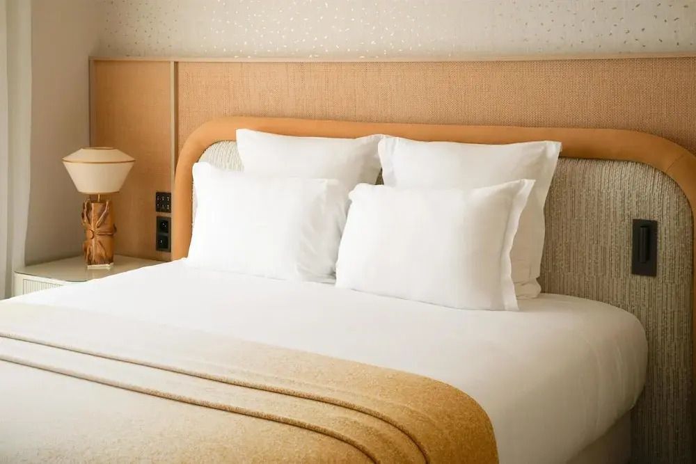 Großes Doppelbett mit weißen Kissen und beiger Bettdecke in einem eleganten Hotelzimmer.