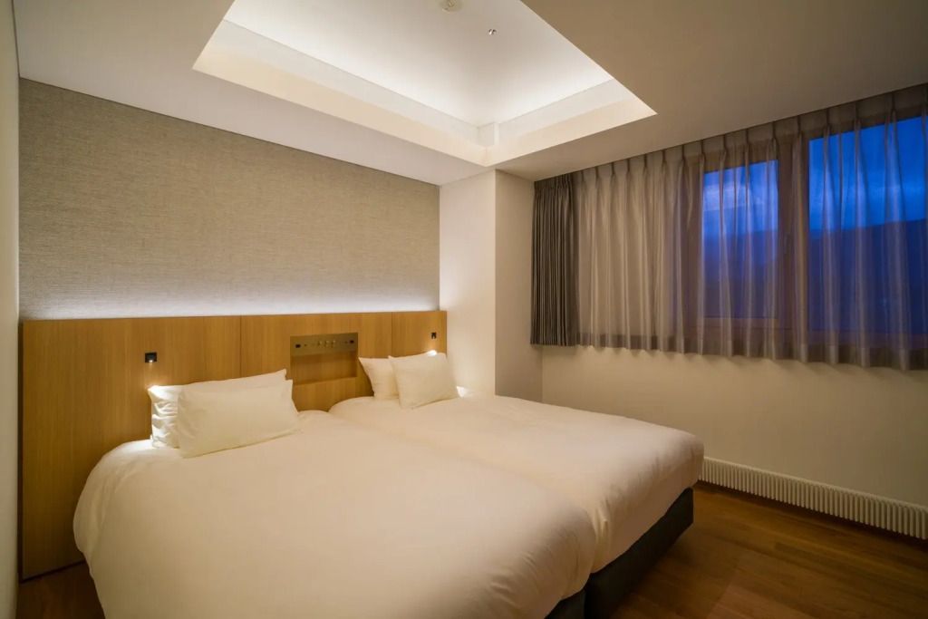 Zimmer mit zwei Einzelbetten, moderner Beleuchtung und Vorhang am Fenster